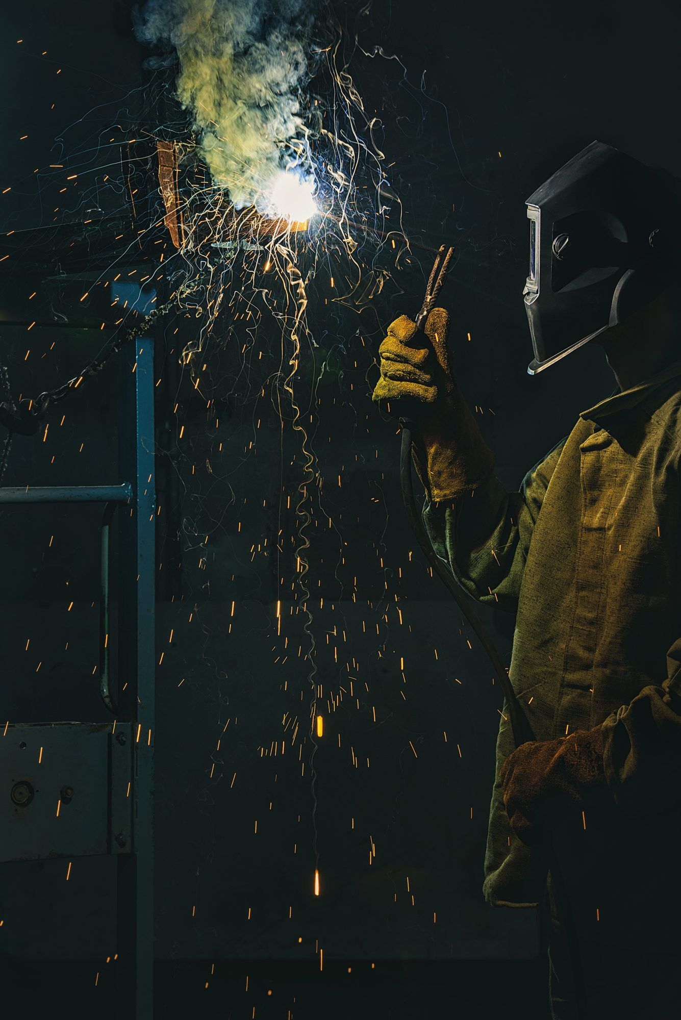 A welder in a protective helmet and gloves working in a dark shop